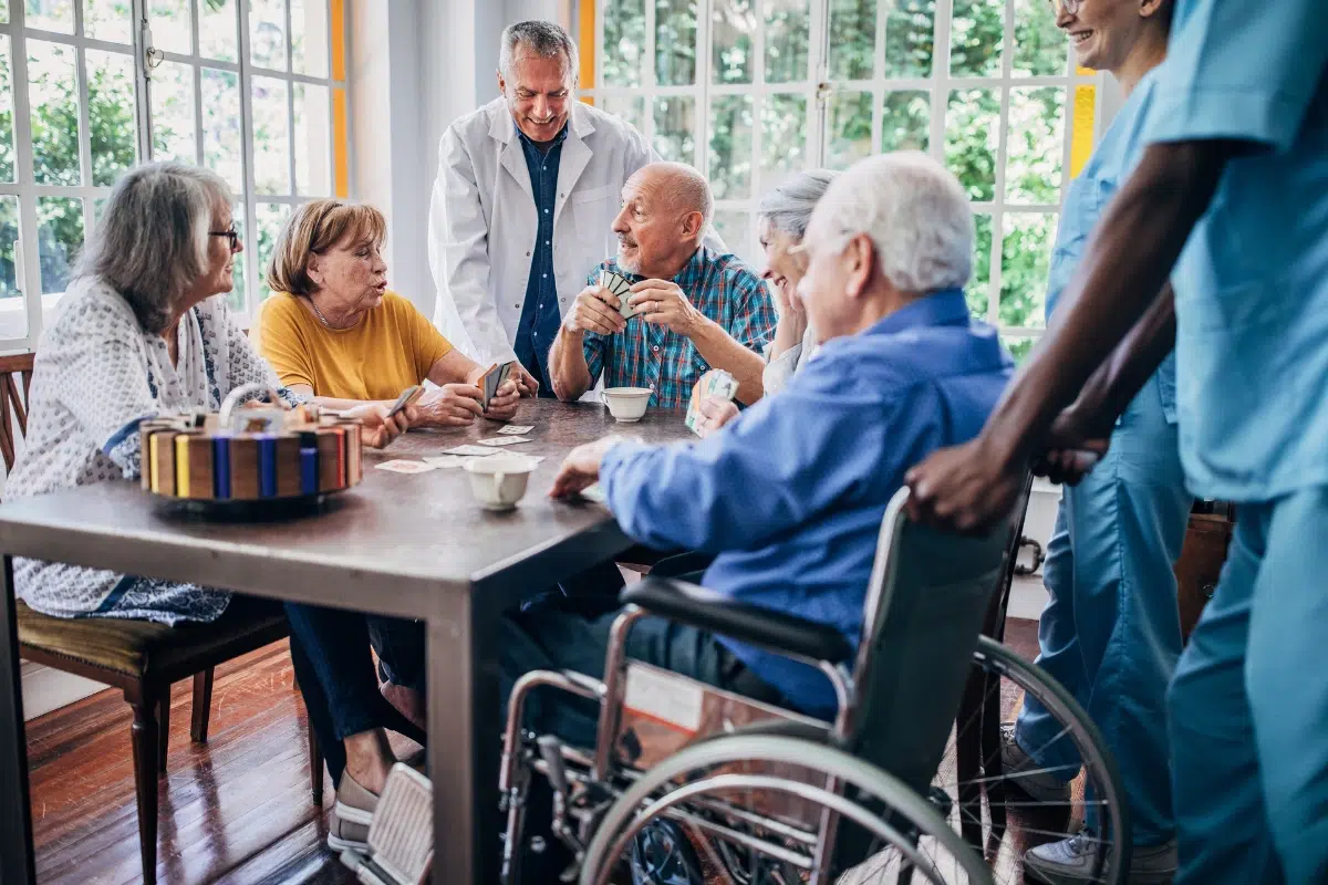 groupe de seniors autour d'une table entrain de jouer aux cartes dans une maison de france autonomie