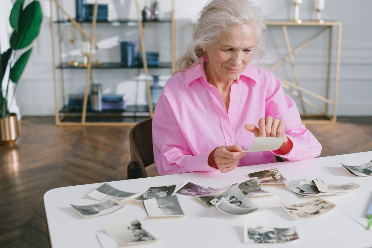 Une dame âgée assisse à la table de son salon entrain de tenir une photo de son enfance