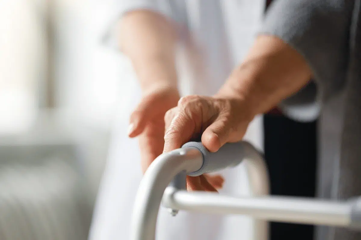 main d'une aide soignante sur la main d'une résidente d'ehpad tenant son déambulateur