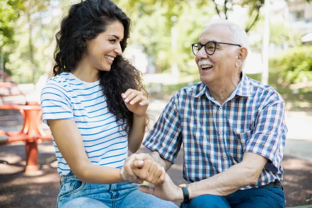 Un senior souriant accompagné de sa fille dans un jardin lumineux illustrant la bienveillance et le lien familial